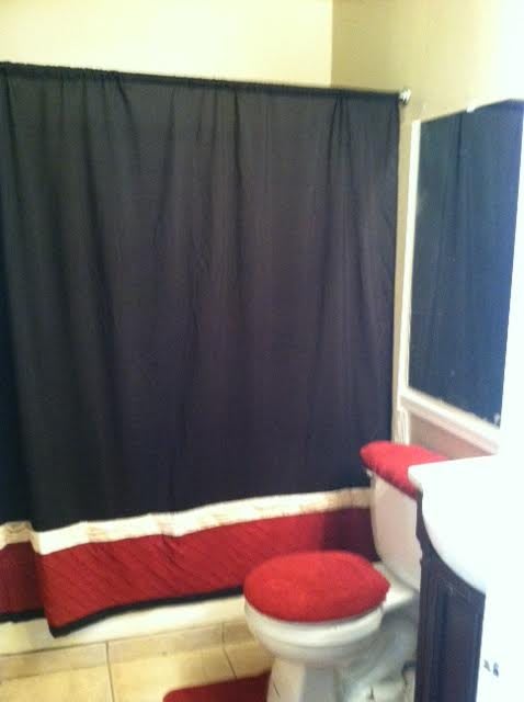 A bathroom with a black and red color scheme, featuring a shower curtain and toilet cover.