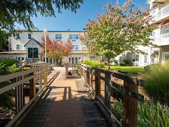 A scenic view of a building with a wooden bridge and lush trees on a sunny day.