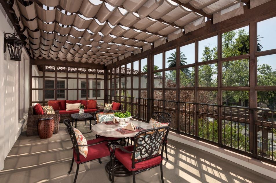 A cozy outdoor patio with a pergola, featuring a dining set with red-cushioned chairs and surrounding seating.