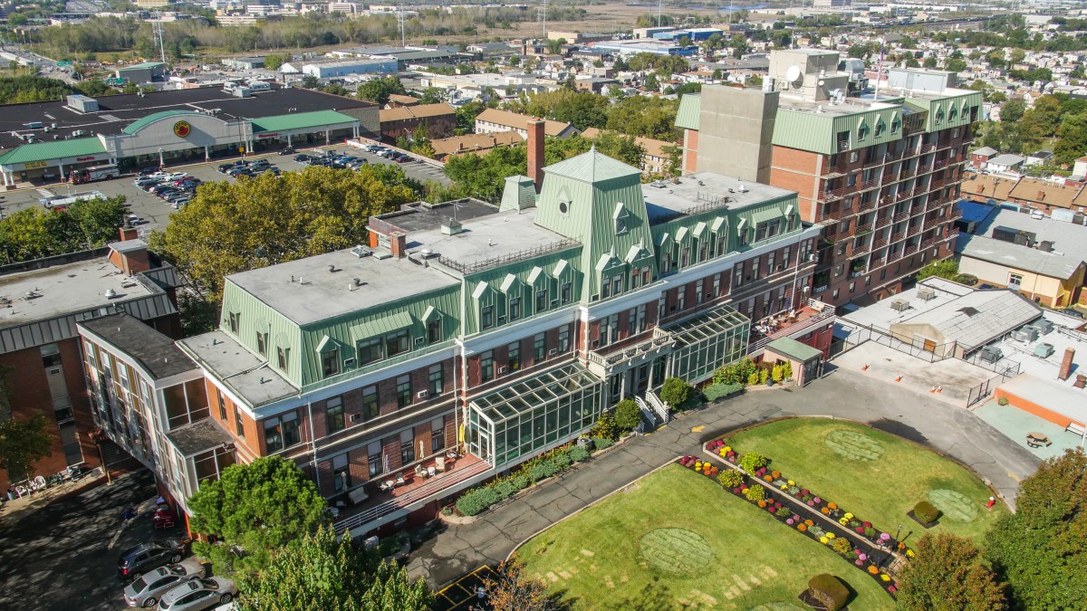 Aerial view of a large building with green rooftops and an adjacent garden in an urban setting.