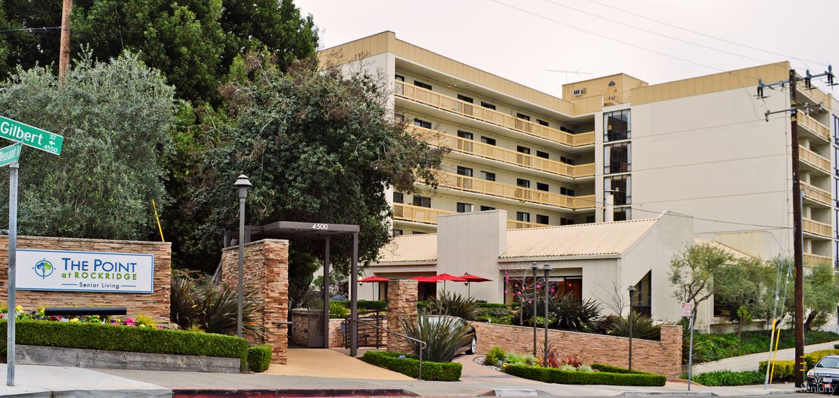 A modern hotel building with balconies, surrounded by trees and landscaping.