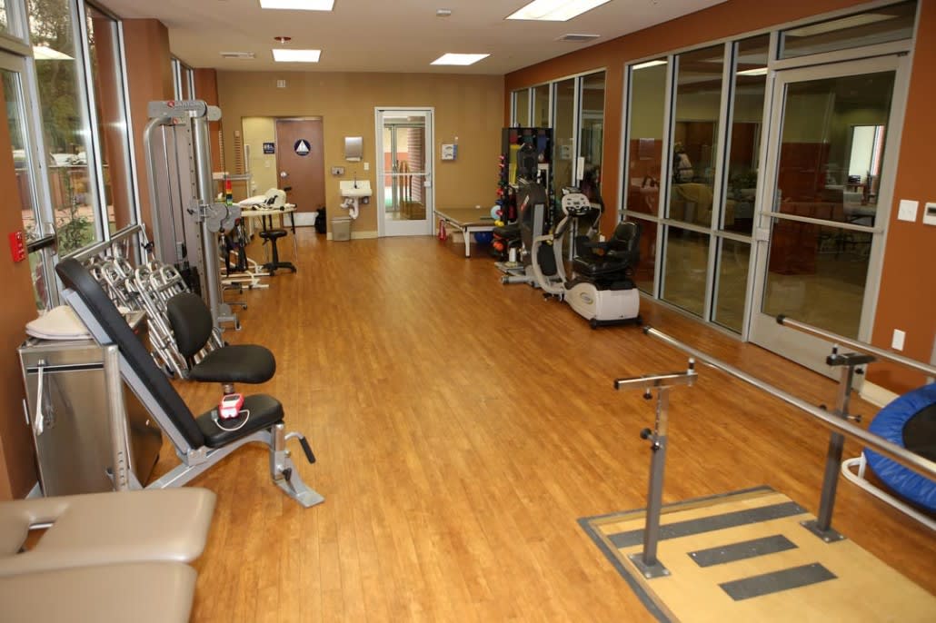 An empty gym with various exercise equipment along a wooden floor.