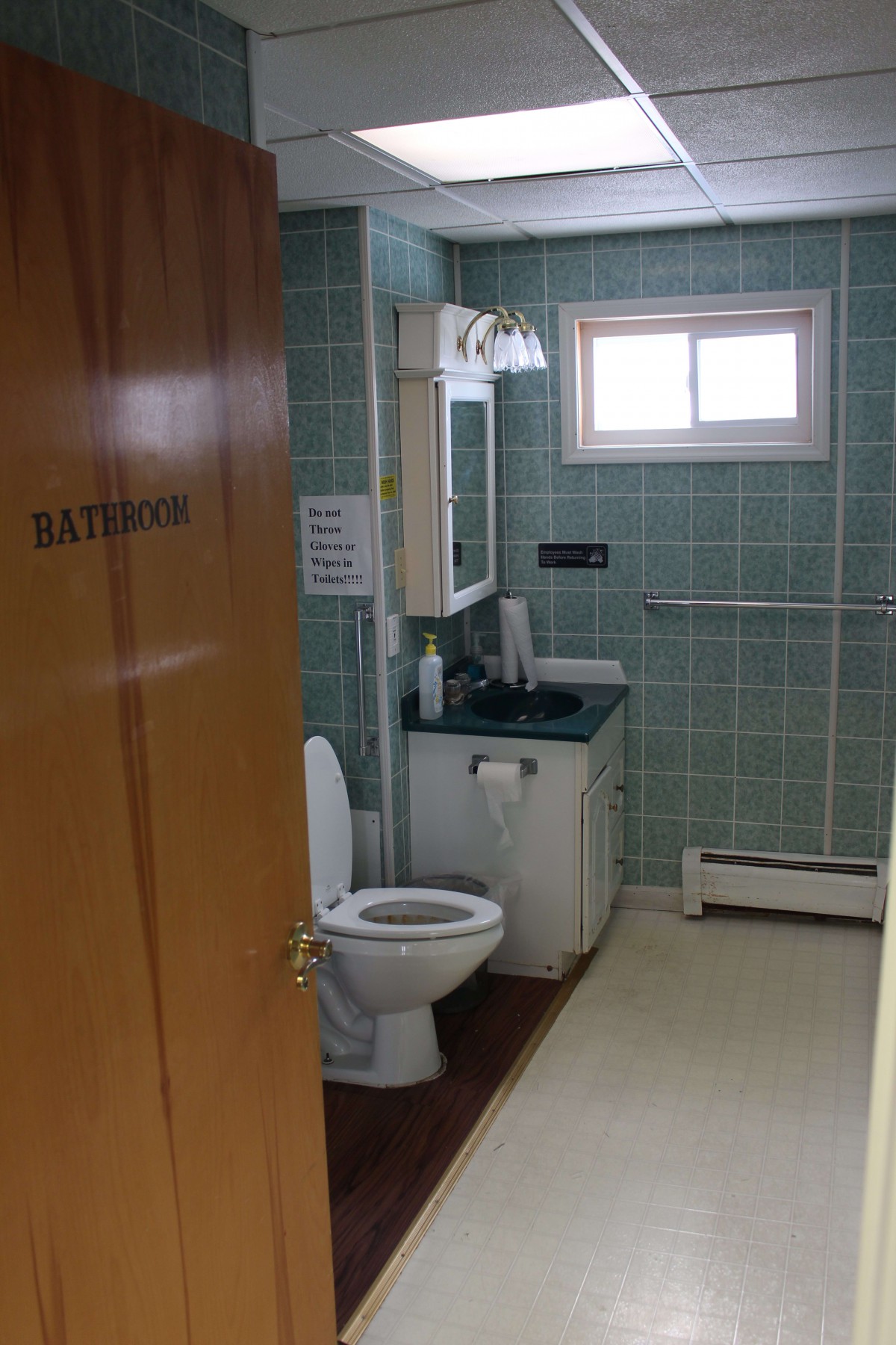 A bathroom with a toilet, sink, and mirror, featuring tiled walls and a small window.