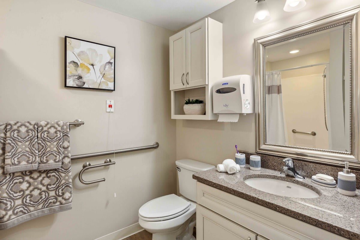 A clean and organized bathroom with a toilet, sink, mirror, and storage cabinets.