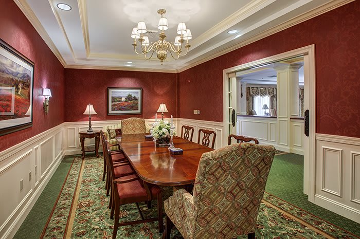 A traditional dining room with a wooden table, red walls, and an elegant chandelier.