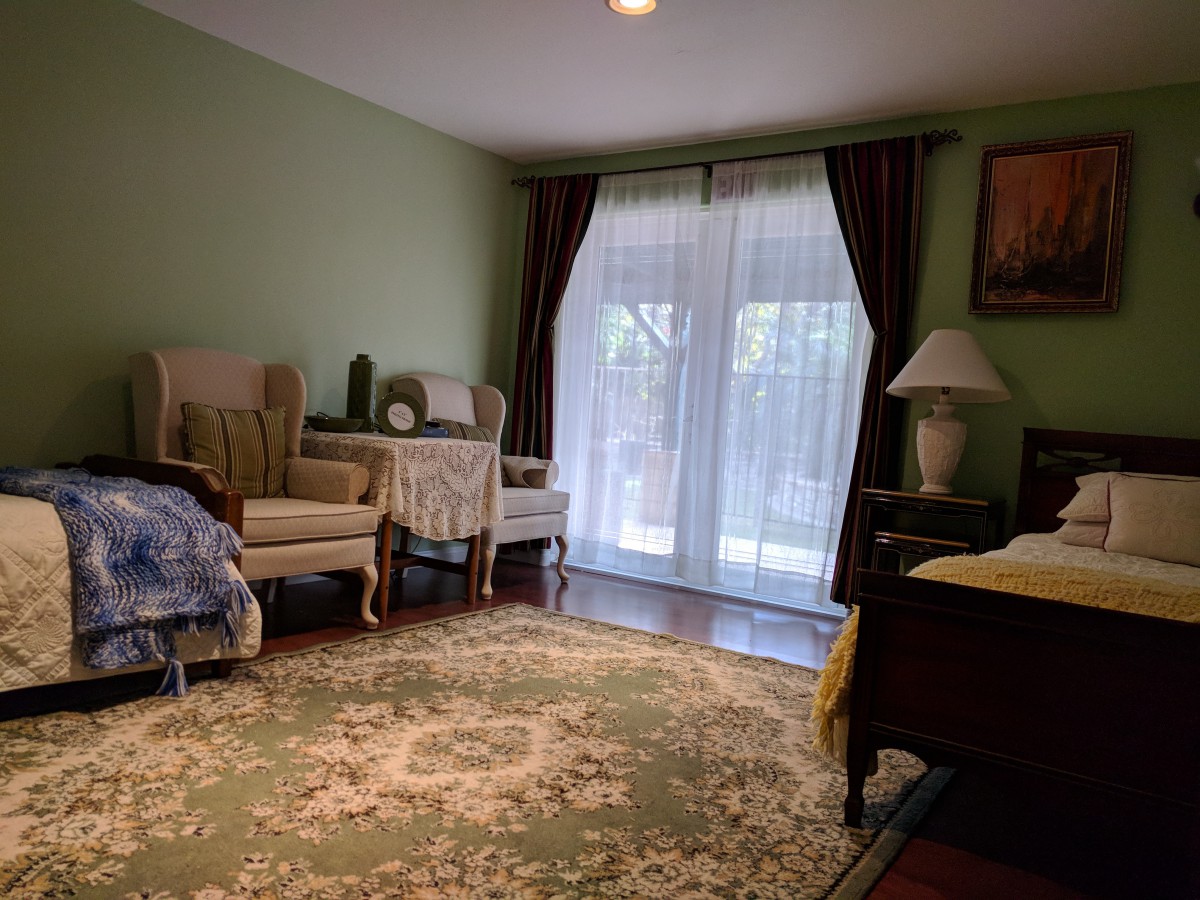 A cozy living room with armchairs, a patterned rug, and a table lamp near a large window with curtains.