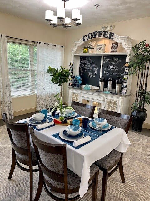 A cozy dining area with a neatly set table and a charming coffee station, surrounded by plants and natural light.