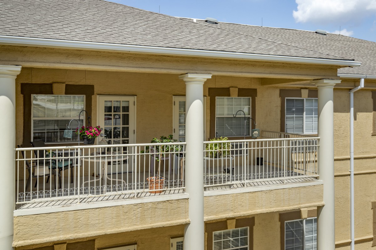 A view of a residential apartment balcony with outdoor seating and decorative plants.