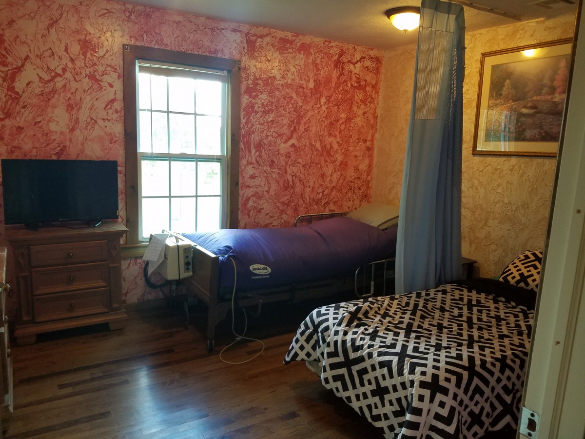 A cozy bedroom with two beds separated by a curtain, featuring a window and television.