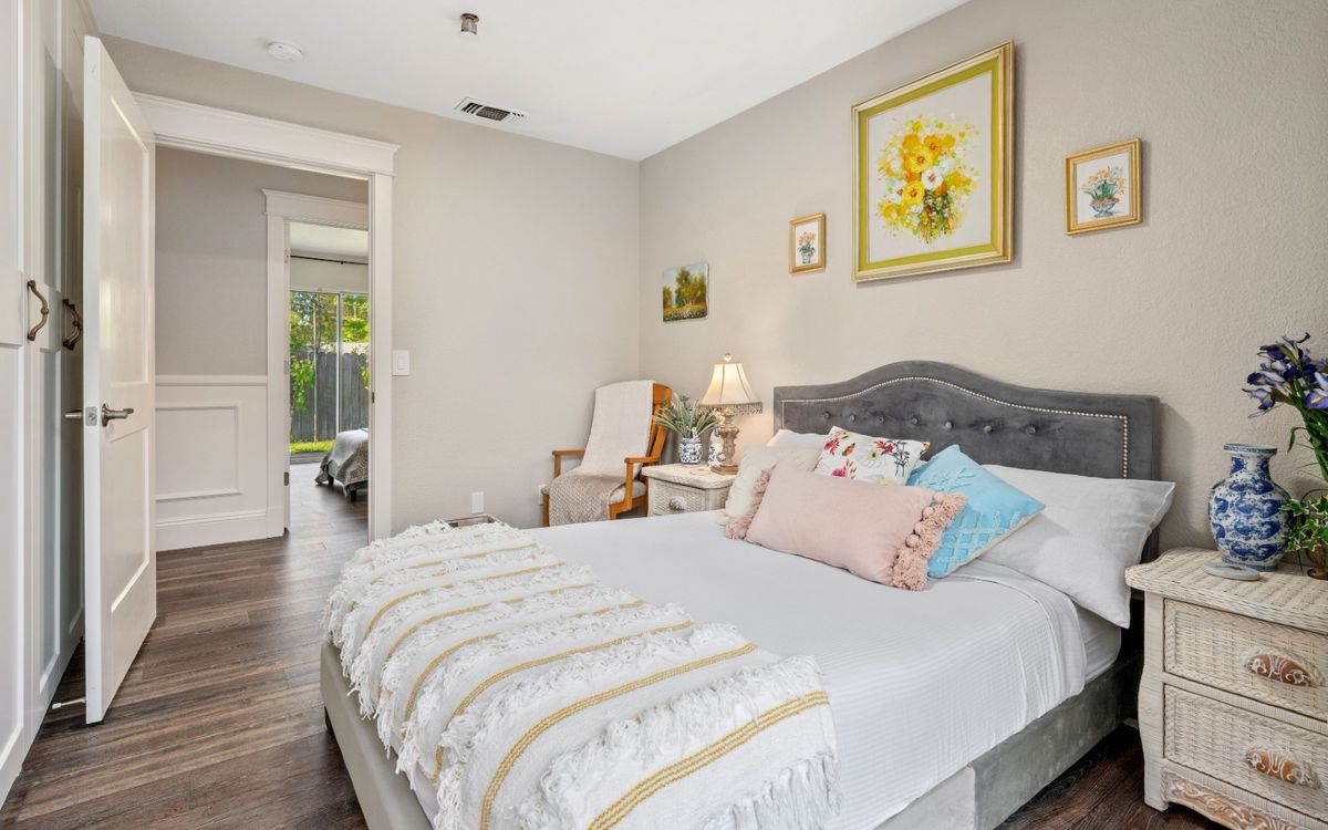 A cozy bedroom with stylish decor, featuring a bed with colorful pillows and wall paintings.