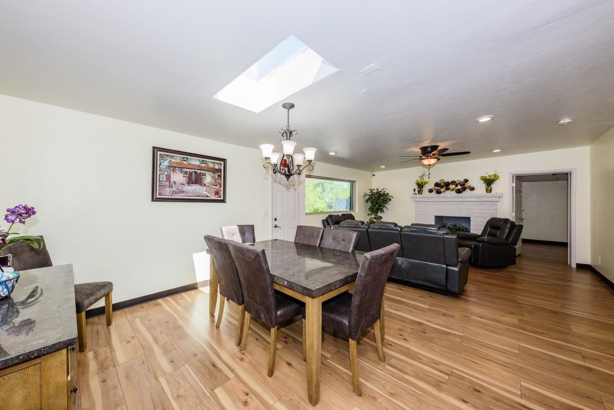 A modern open-concept dining and living area with hardwood floors, featuring a large table, comfortable seating, and natural light from a skylight.