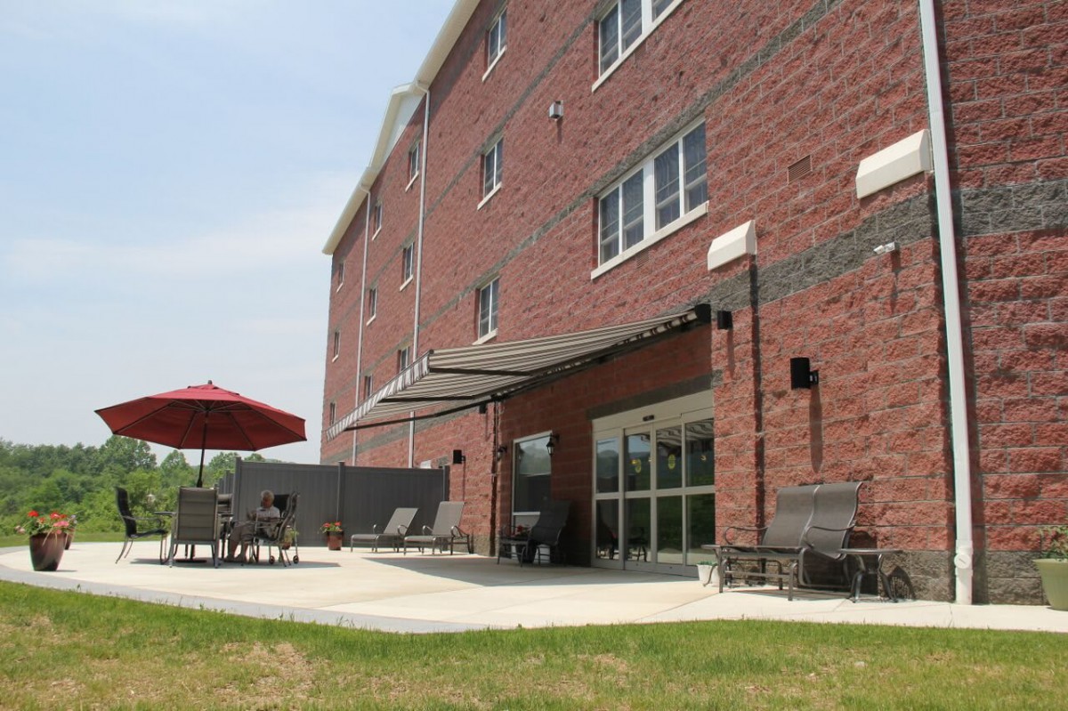A brick building with an outdoor patio featuring chairs and a red umbrella.