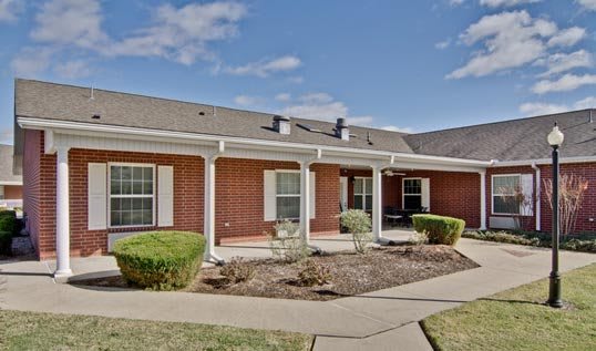 A suburban one-story brick house with a porch and landscaped yard.
