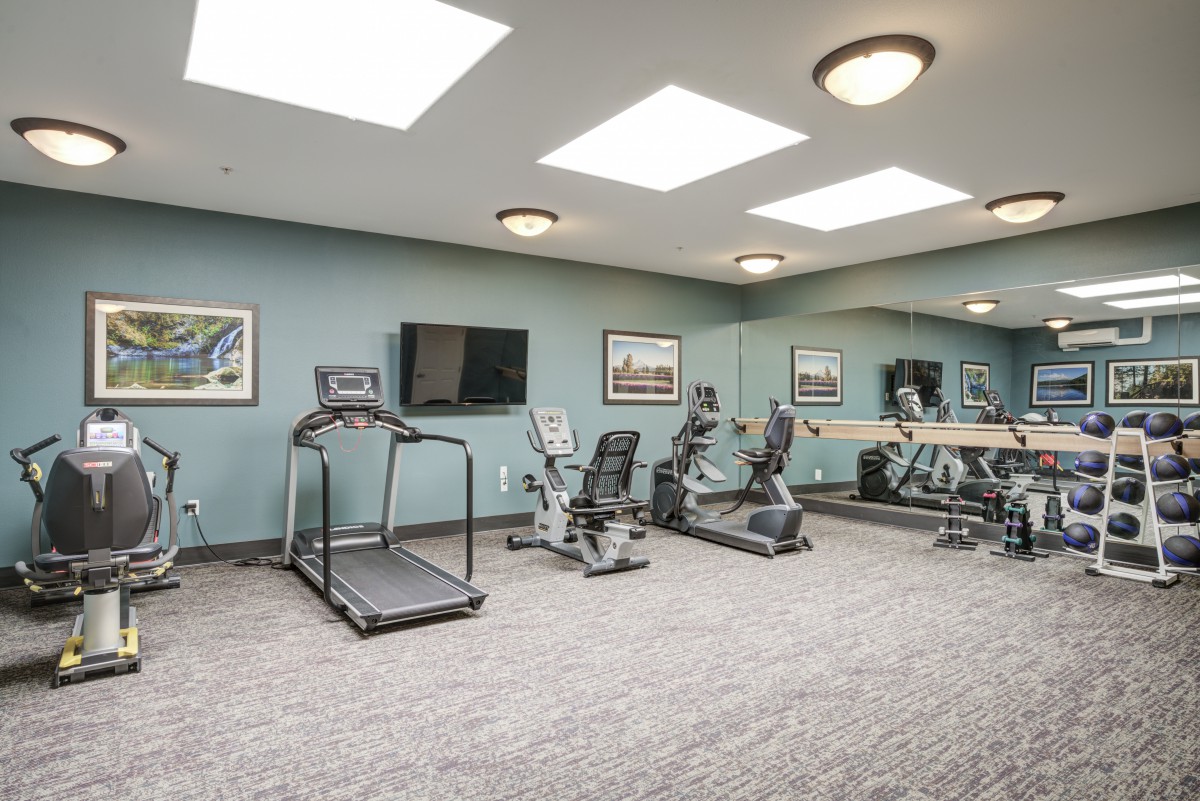 A modern indoor gym with various exercise equipment including a treadmill and stationary bikes.