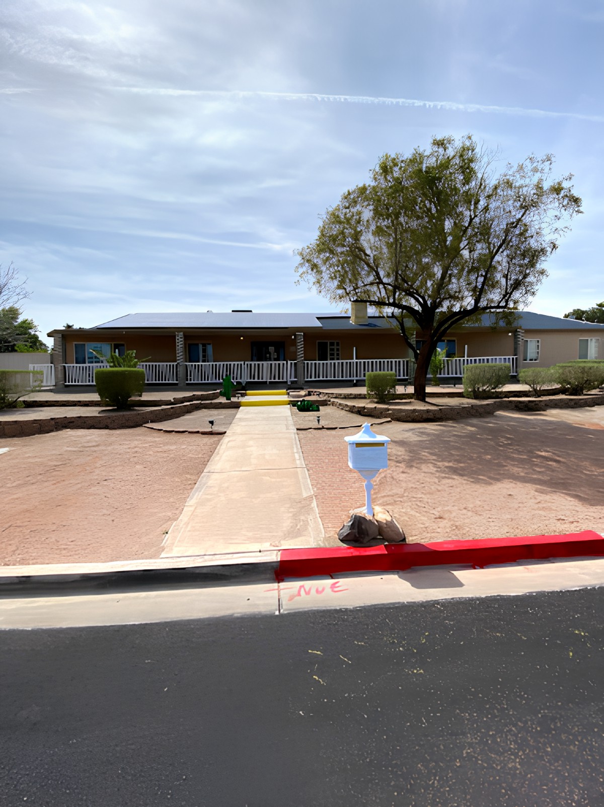 A suburban house with a long driveway, landscaped yard, and surrounding fence.