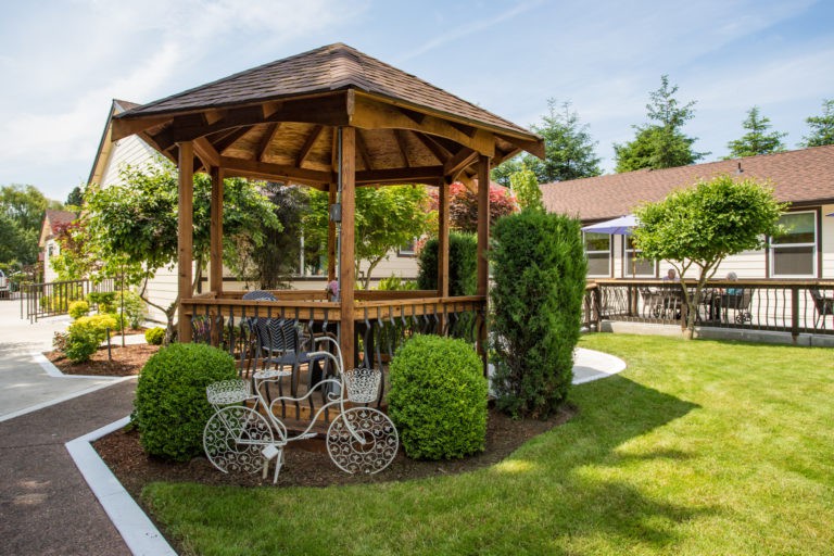 A charming wooden gazebo surrounded by lush greenery and adorned with a decorative bicycle in a well-maintained garden setting.