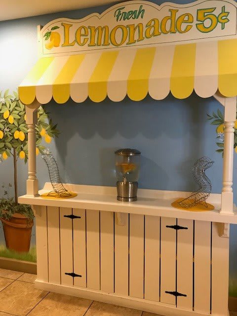 A charming lemonade stand with a yellow and white striped awning, complete with decorative lemons and drink dispensers.