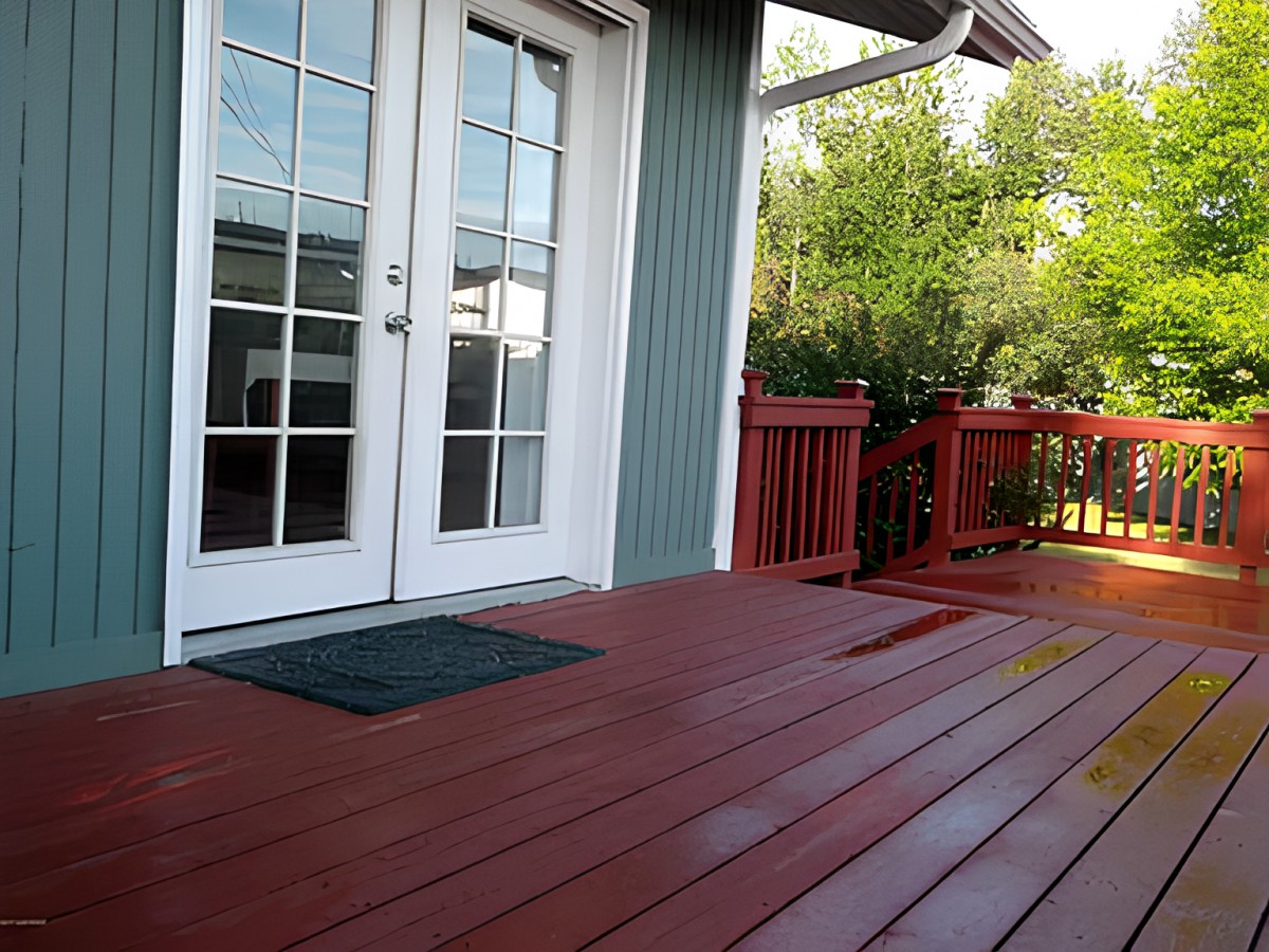 A wooden patio with red railings and French doors leading to the house.