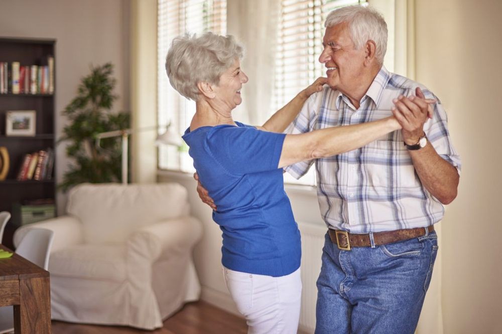 An elderly couple joyfully dancing together at home.