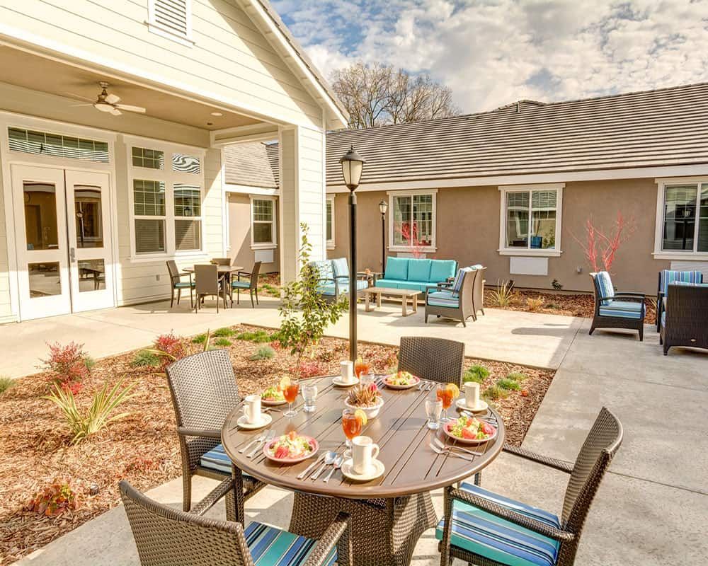 A modern outdoor patio with a dining table set for guests on a sunny day.
