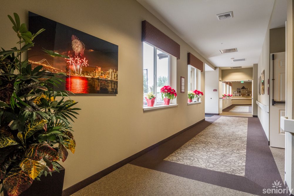 A well-lit hallway featuring artwork on the wall and flowers by the windows.