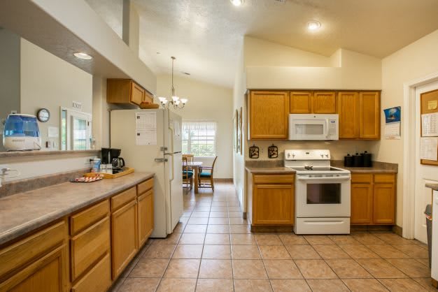 A modern kitchen with wooden cabinets, tiled flooring, and a dining area in the background.
