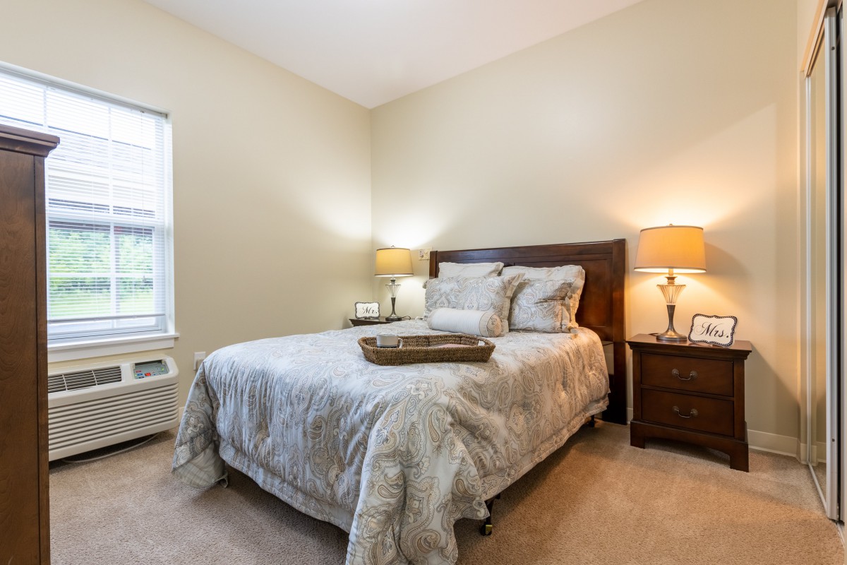A cozy bedroom with a neatly made bed, bedside lamps, and a window providing natural light.