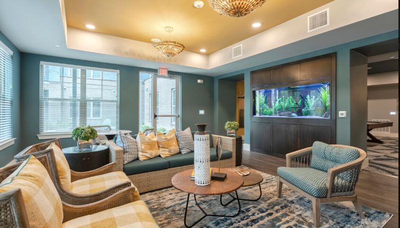 A modern living room with stylish seating, a central coffee table, elegant chandeliers, and an illuminated aquarium.