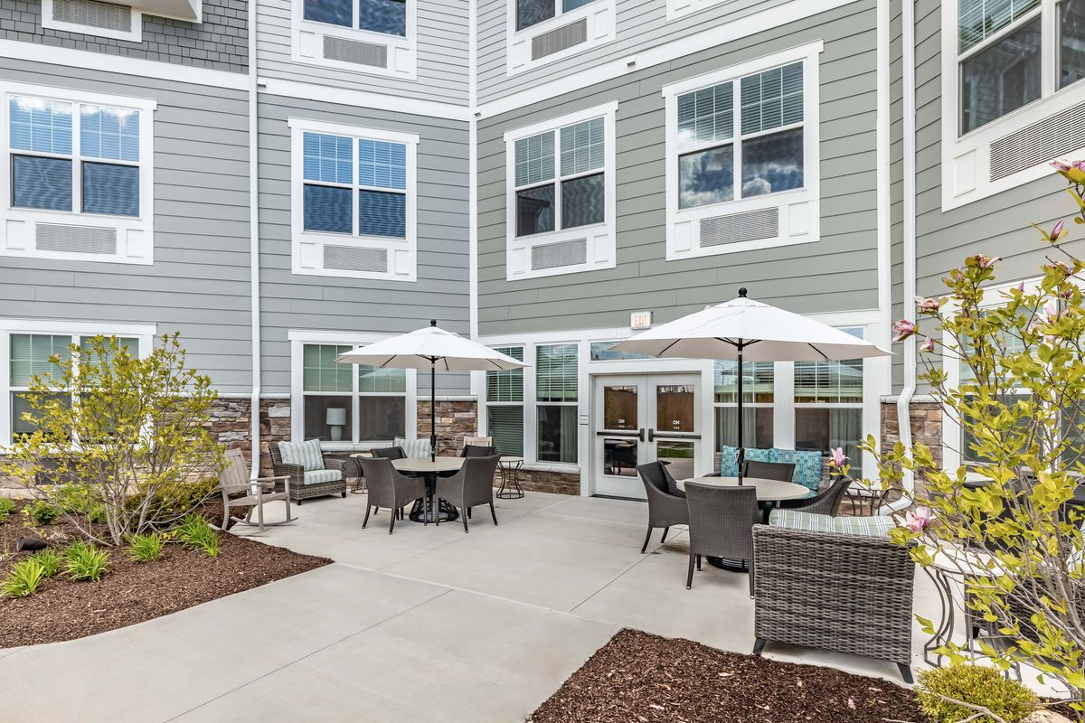 A cozy outdoor patio area with tables, chairs, and umbrellas adjacent to a residential building.