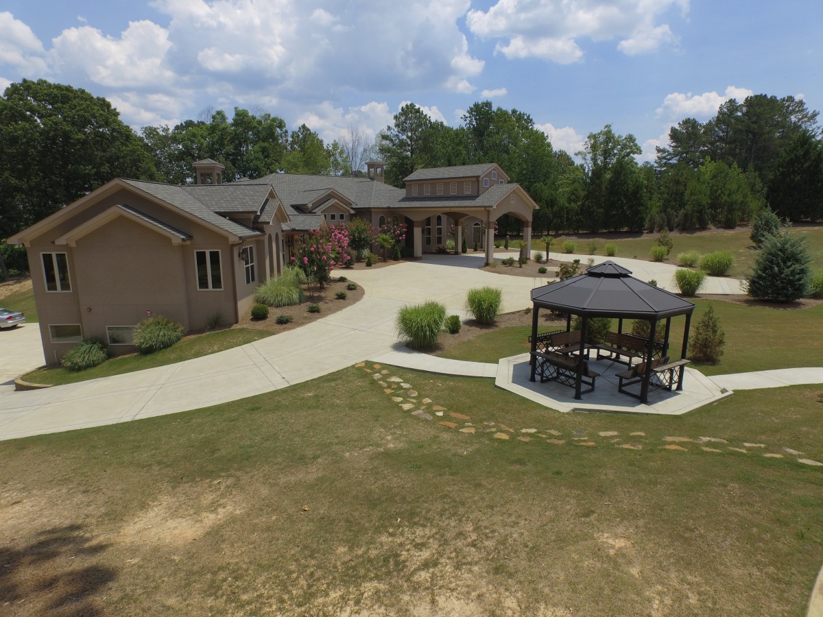 A spacious house with a curved driveway and nearby gazebo, surrounded by trees and landscaping under a partly cloudy sky.