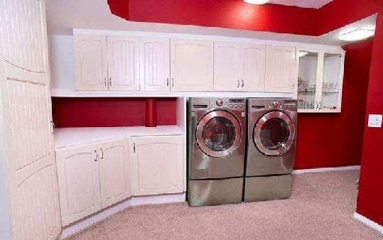 A modern laundry room featuring a washer and dryer set, surrounded by white cabinets and a red accent wall.