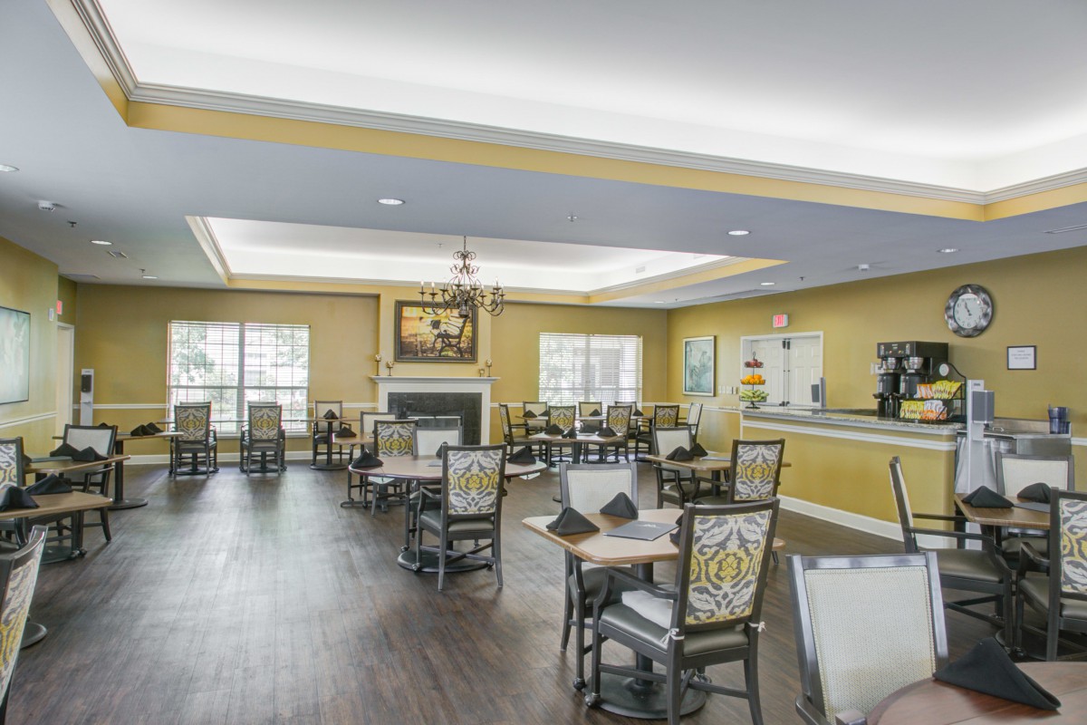 A well-lit dining room with elegant decor, featuring multiple tables and chairs, a fireplace, and large windows.