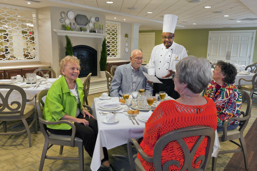 A group of elderly people enjoying a meal in a restaurant while a chef presents the menu.
