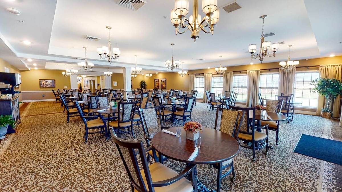 A spacious dining room with elegantly set tables and chairs, featuring traditional chandeliers.
