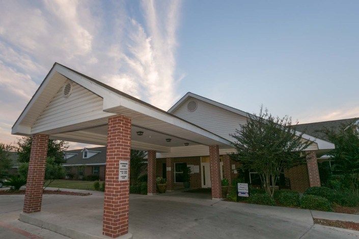 Entrance of a brick and white-paneled building with a clear sky and clouds above.