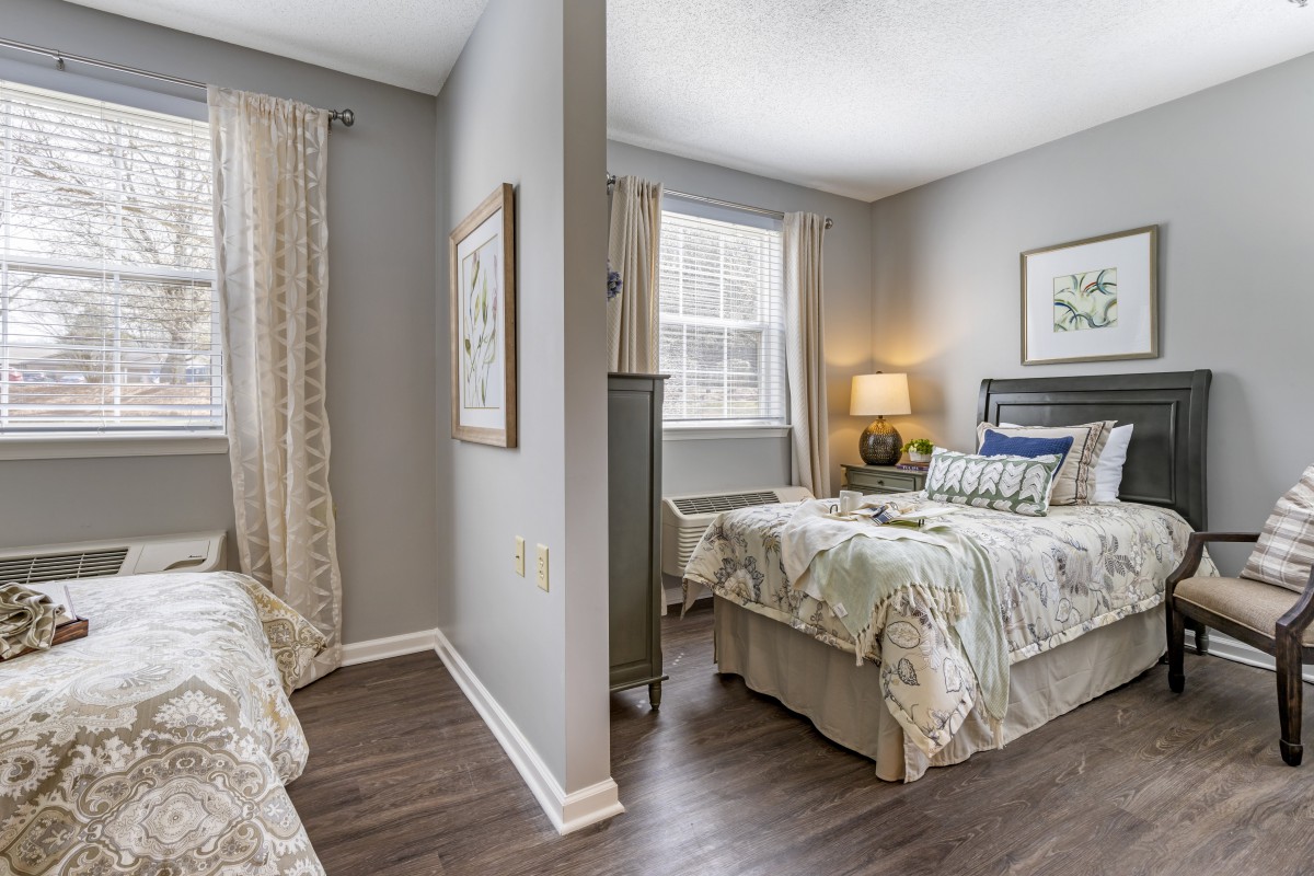 A cozy bedroom with twin beds separated by a partial wall, featuring neutral colors and elegant decor.