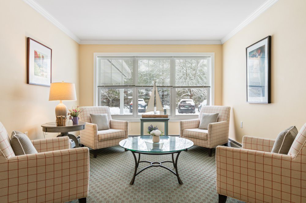 A cozy living room with comfortable armchairs and a coffee table, illuminated by natural light from a large window.
