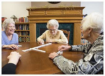 A group of elderly individuals playing dominoes at a table in a cozy room.