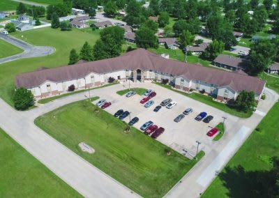 Aerial view of a building with a parking lot surrounded by greenery in a residential area.