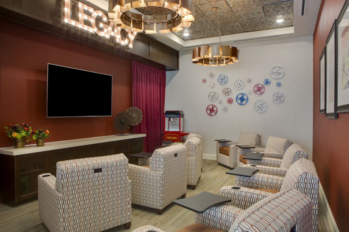 A cozy home theater room with plush seating, a large television, and elegant chandeliers, complemented by decorative wall art.