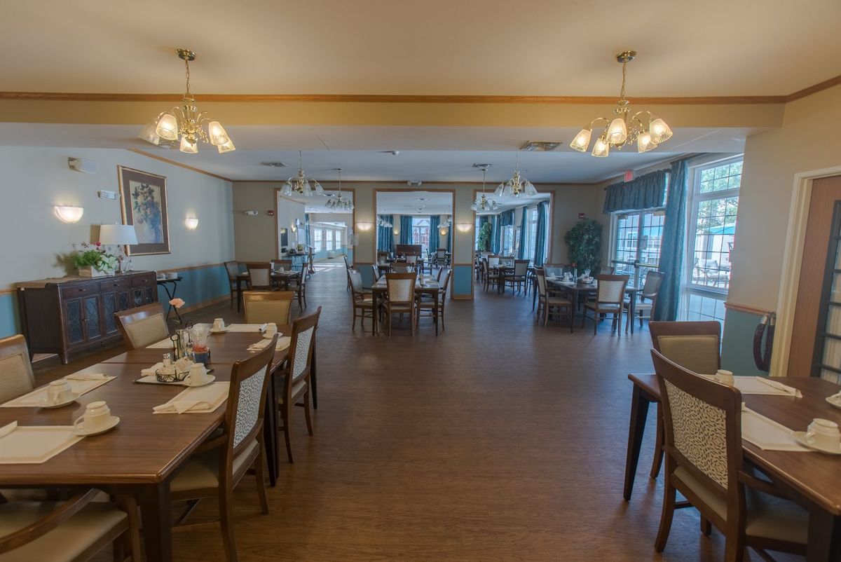 A spacious dining area with neatly arranged tables and chairs, featuring elegant chandeliers and large windows.