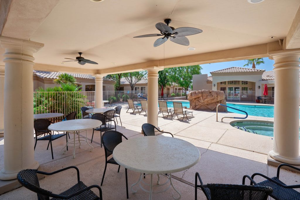 A cozy outdoor patio with tables and chairs overlooking a swimming pool.