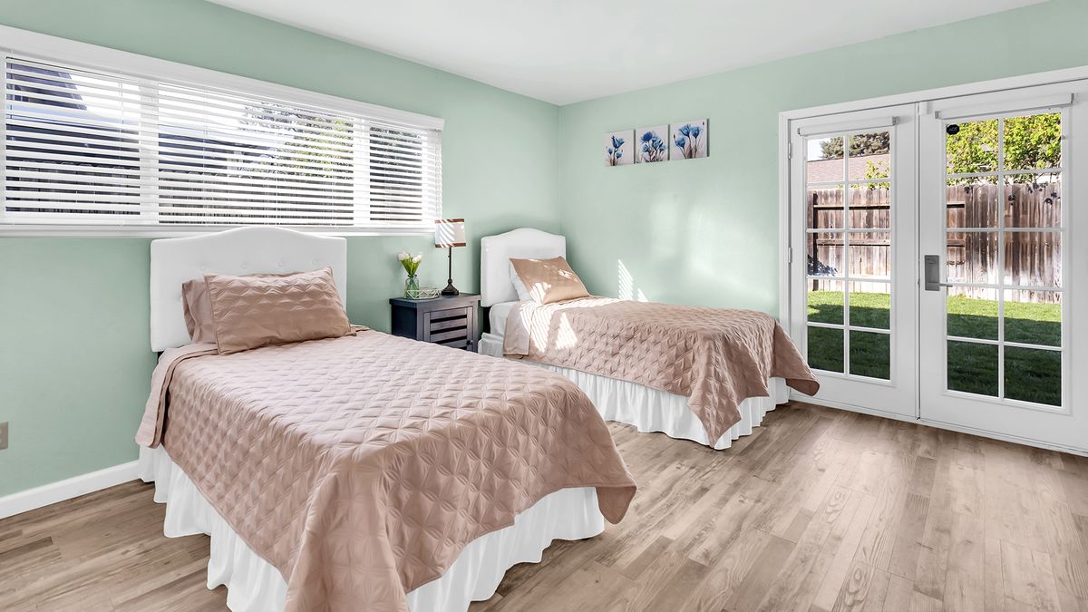 A bright and modern bedroom featuring two twin beds with beige covers and light wood flooring.