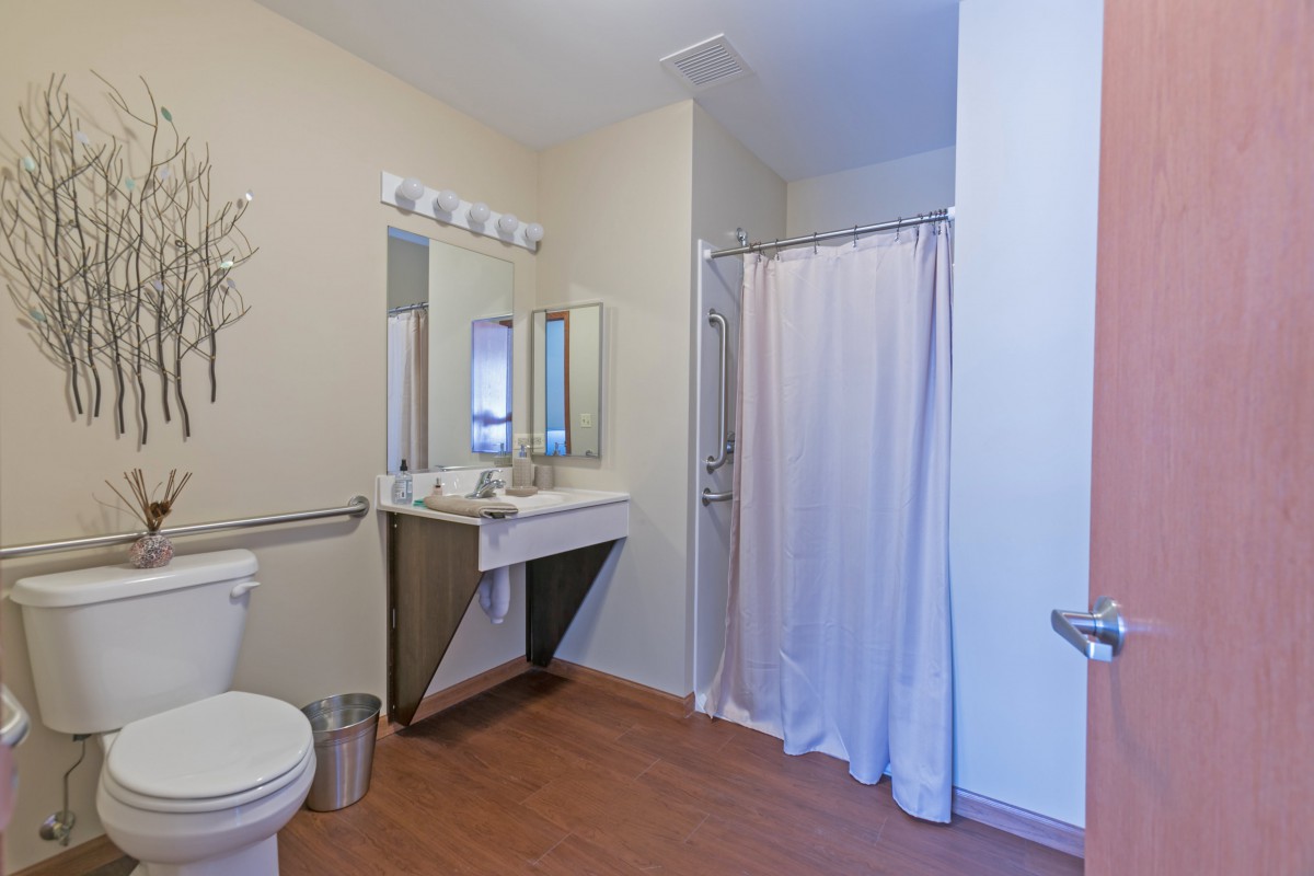 A spacious bathroom featuring a sink with a mirror, a shower with a curtain, and a toilet.