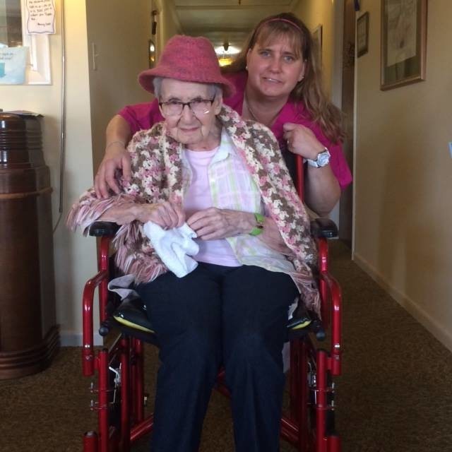 A caregiver assisting an elderly woman in a wheelchair.