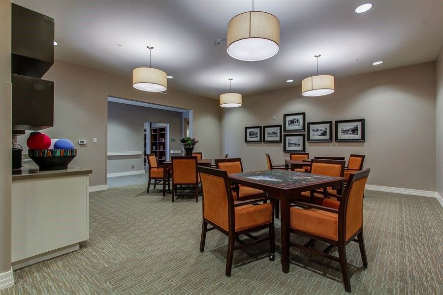 A modern dining room with elegant lighting and vibrant orange chairs surrounding dark wood tables.