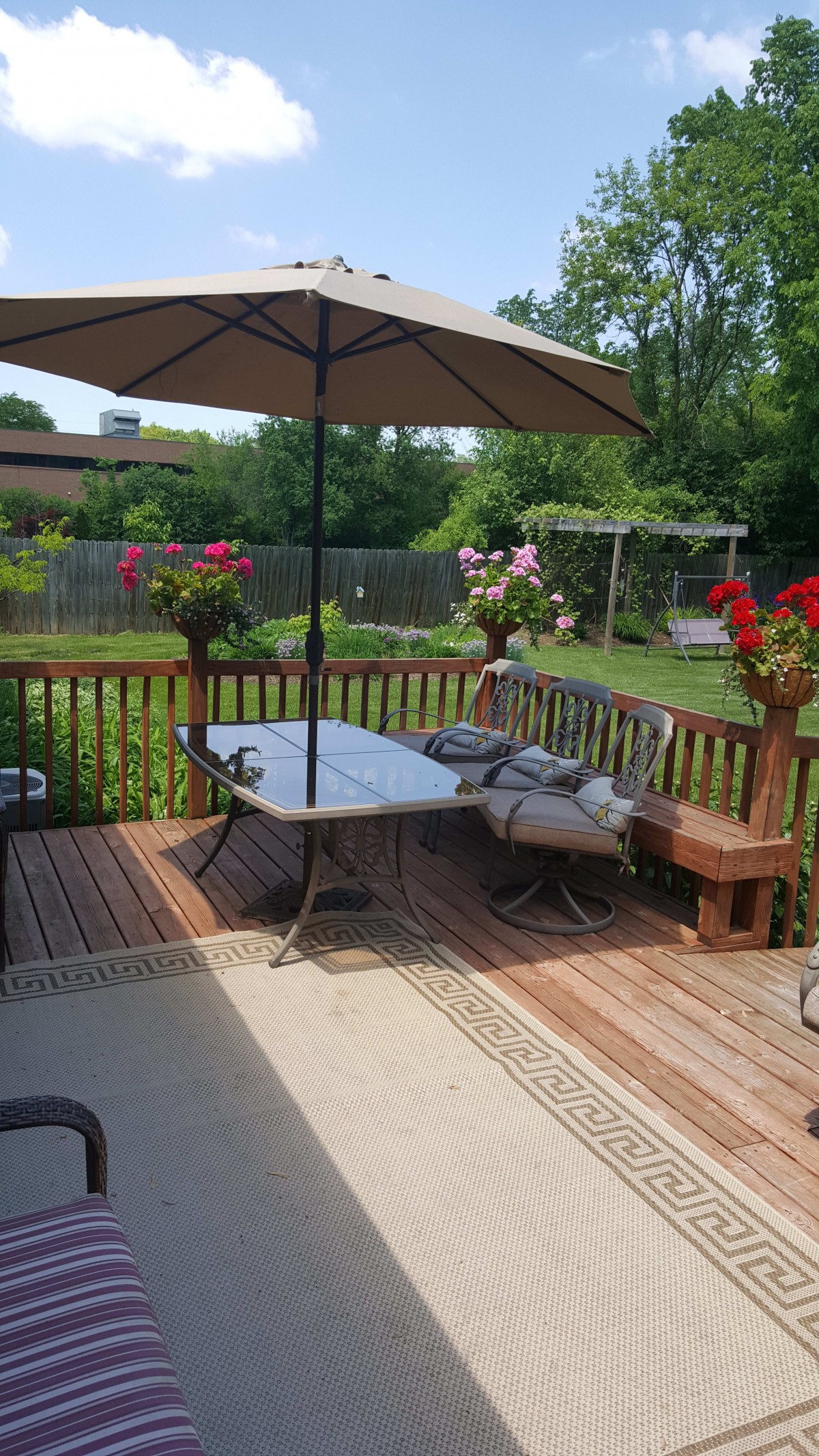 A cozy backyard deck with a table and umbrella, surrounded by vibrant flowers.