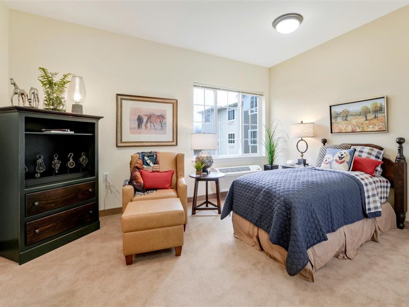 A cozy bedroom with a comfortable armchair, neatly made bed, and decorative artwork on the walls.