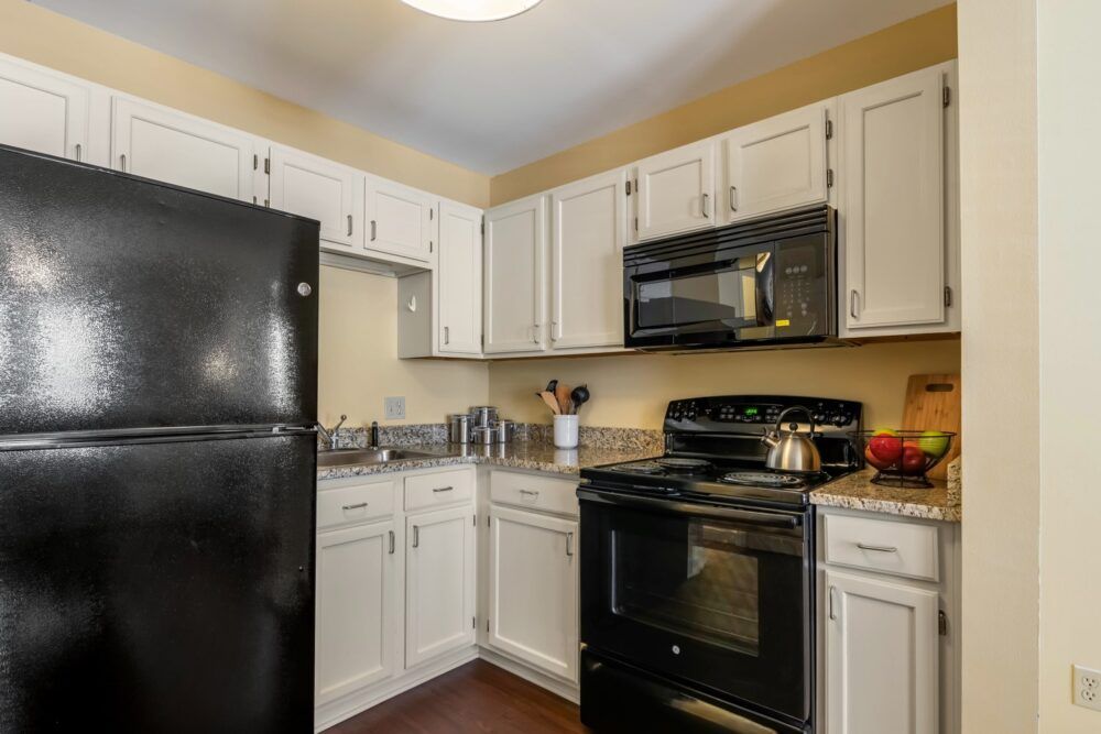 A modern kitchen with white cabinets and black appliances, featuring a stove, refrigerator, and microwave.