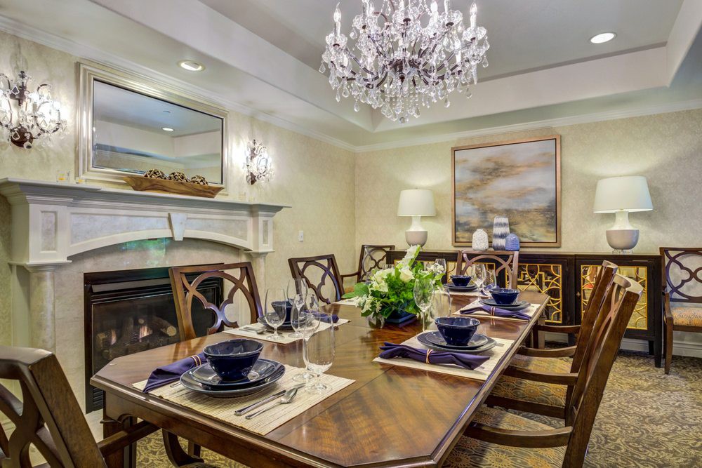 An elegant dining room with a large wooden table set for dinner, a chandelier overhead, and tasteful decor including a fireplace and artwork.
